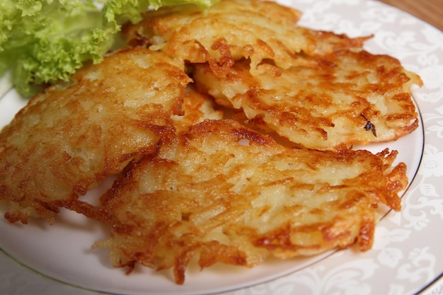 Cooking homemade potato pancakes with green salad on a white plate on a wooden background Vegetarian food concept Closeup