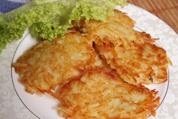 Cooking homemade potato pancakes with green salad on a white plate on a wooden background Vegetarian food concept Closeup