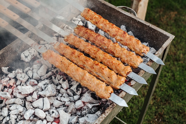 Cooking kebab meat with skewers on grill.