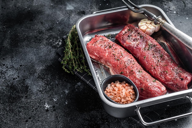 Cooking Lamb tenderloin fillet meat with herbs and olive oil marinated mutton meat in kitchen tray Black background Top view Copy space