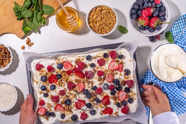 Cooking making Frozen Yogurt Bark background with greek yogurt fresh berry granola honey chocolate sauce with baking tray deco Top view of woman hands cook frozen yoghurt bars