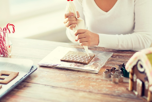 cooking, people, christmas and decoration concept - close up of happy woman making gingerbread houses at home