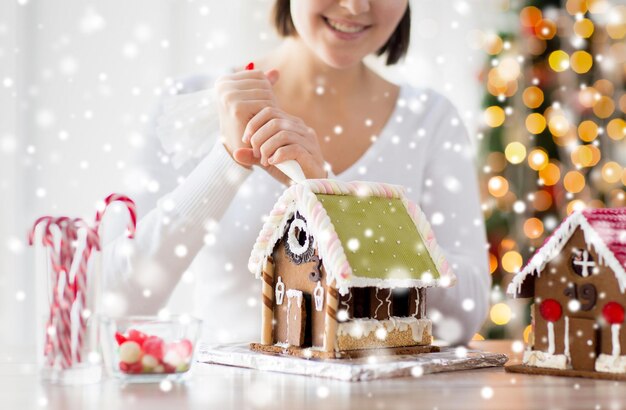 cooking, people, christmas and decoration concept - happy woman making gingerbread houses at home