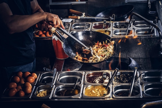 Cooking process in an Asian restaurant. Cook is fry vegetables with spices and sauce in a wok