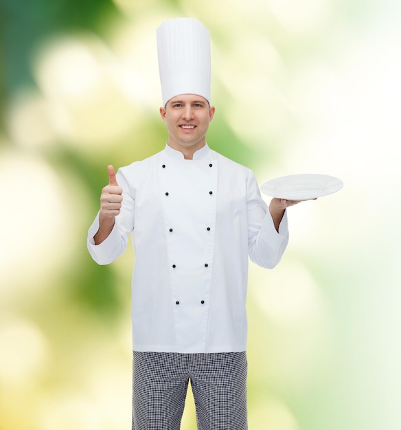 cooking, profession, advertisement and people concept - happy male chef cook holding something on empty plate and showing thumbs up over green background