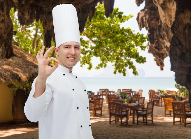 cooking, profession, gesture and people concept - happy male chef cook showing ok sign over restaurant lounge on beach