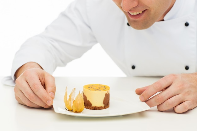 cooking, profession, haute cuisine, food and people concept - close up of happy male chef cook decorating dessert