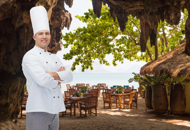 cooking, profession and people concept - happy male chef cook with crossed hands over restaurant lounge on beach