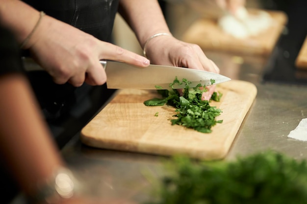 cooking in a restaurant chef's hand cutting greens on a wooden board