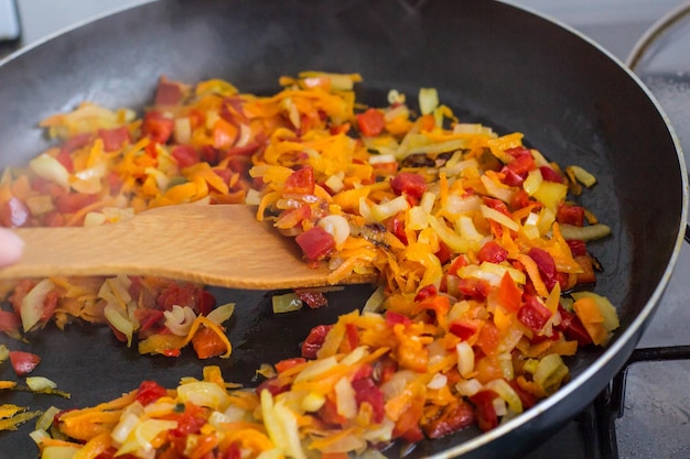 Cooking a roast for soup of onions carrots paprika tomatoes herbs and spices in sunflower oil in a frying pan