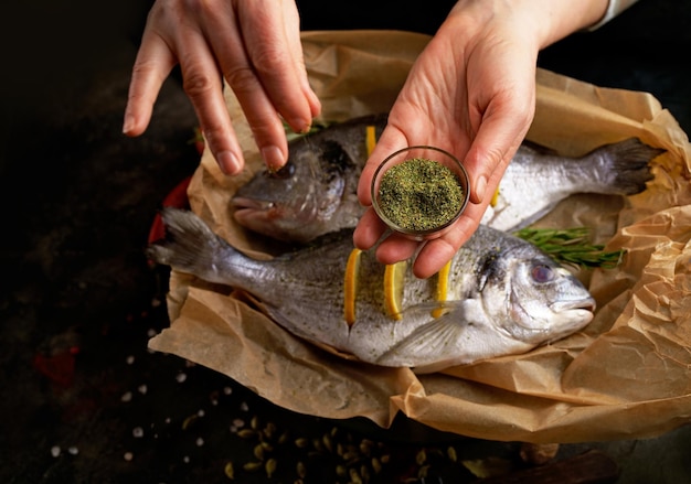 Cooking sea fish Fresh ready to cook raw bream fish dorado with ingredients and seasonings like rosemary salt pepper lime and olive oil top view