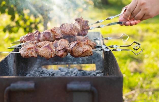 Cooking shish kebab on the grill with smoke the man flips the skewers Fresh meat for barbecue grilled on fire Picnic in nature