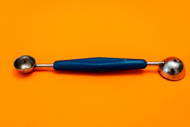 Cooking spoon to make little balls with vegetables or fruits like noisette potatoes with orange background Kitchen and pastry utensil