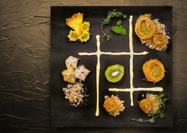 Photo cooking sweets turkish traditional ramadan pastry dessert kunafa (kadaif, baklava),kiwi,ananas,nuts ,dark  background.plate art composition.