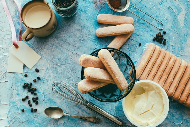 Cooking tiramisu concept, ingredients for making italian dessert on blue table, process of preparation