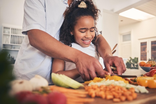 Cooking vegetables and father with kid in the kitchen for child development teaching and learning Bonding happy and dad helping girl to cut ingredients for a dinner supper or lunch meal at home