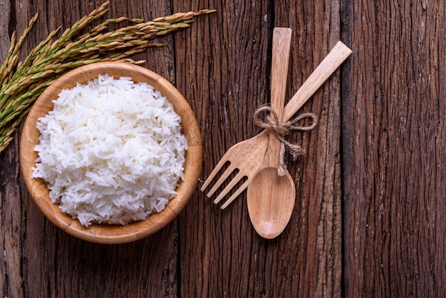 Cooking white rice (Thai Jasmine rice) in wooden bowl with unmilled rice on old wooden bac