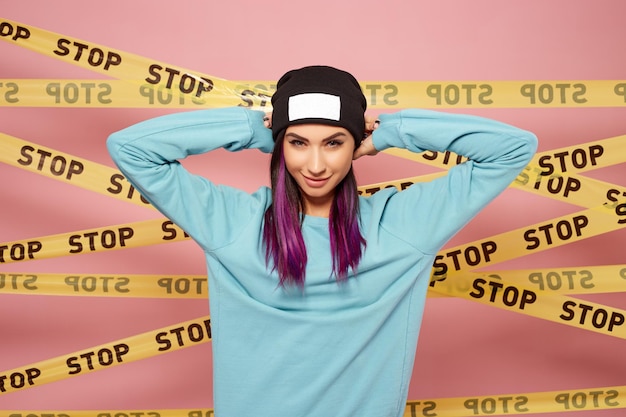 Cool girl with purple hair stands on the background of pink wall with the yellow tapes stop