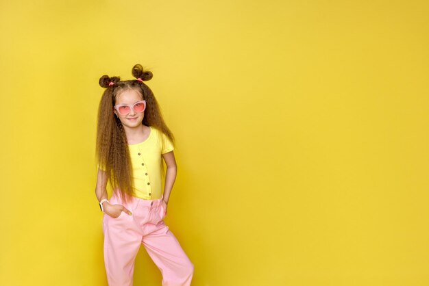 Cool girl with a trendy hairstyle and pink sunglasses with bright emotions on a yellow background