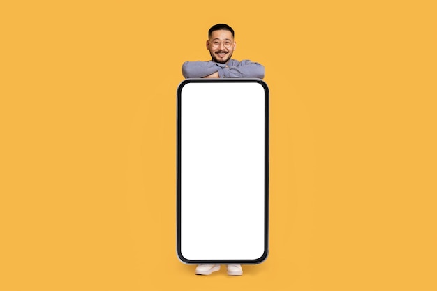 Cool mobile app cheerful asian man demonstrating big smartphone with blank screen