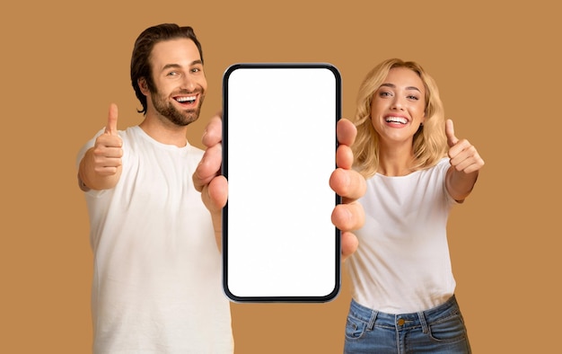 Cool Offer Happy Young Couple Showing Blank Smartphone And Gesturing Thumbs Up