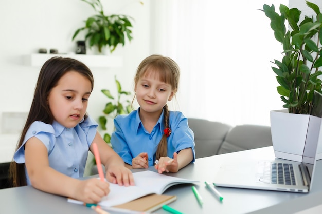 Cool online school. Kids studying online at home using a laptop. Cheerful young little girls using laptop computer studying through online e-learning system. Distance or remote learning