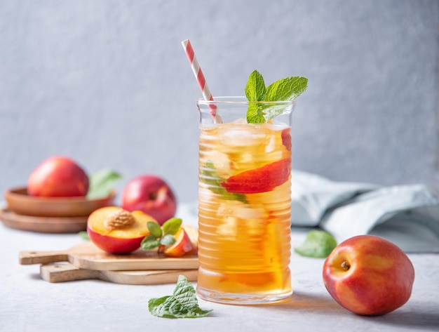 Cool peach tea with mint and ice in a glass on a blue background Front view and copy space image