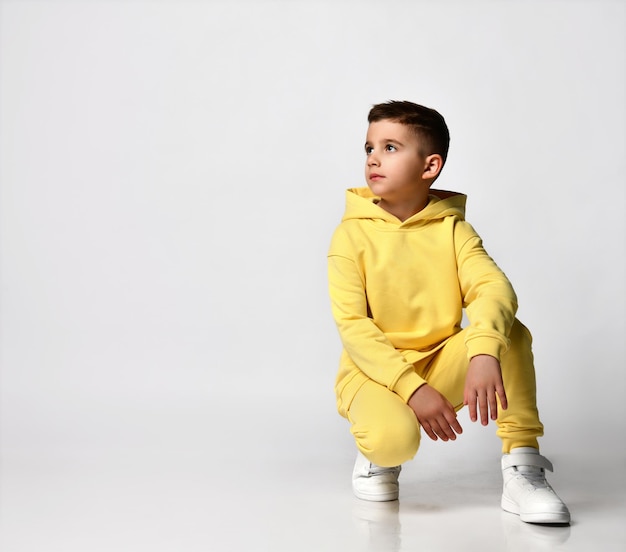 Cool schoolboy in a trendy bright yellow sports suit sitting on a white background