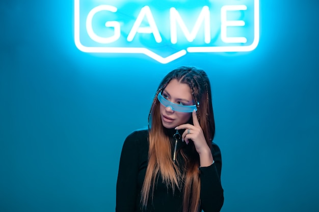 Cool stylish girl with a fashionable hairstyle and stylish glasses with a large glass poses on a bright neon background. High quality photo