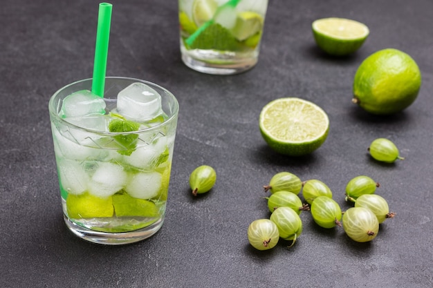 Cooling lemon drink with ice. Straw in glass. Lime on table. Black background. Top view