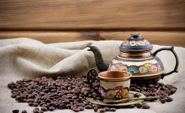 Copper cup and teapot with heap of coffee beans