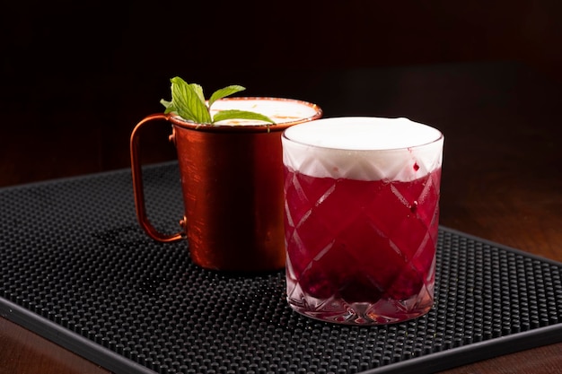 Copper mug of moscow mule drink and berry drink with mint leaves seen from the front on the bar counter