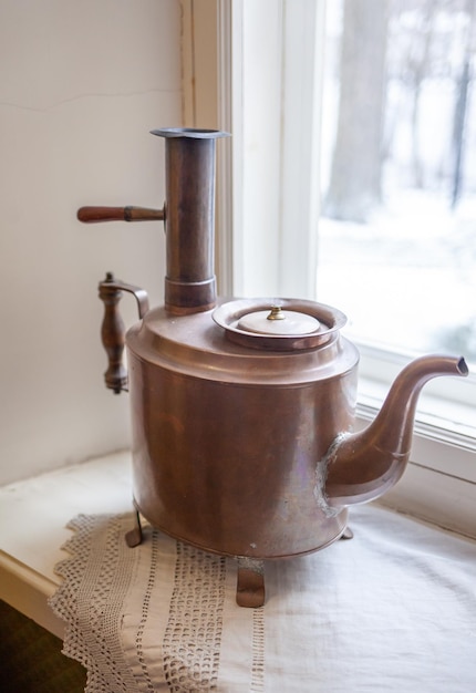 A copper pot sits on a window sill next to a window.