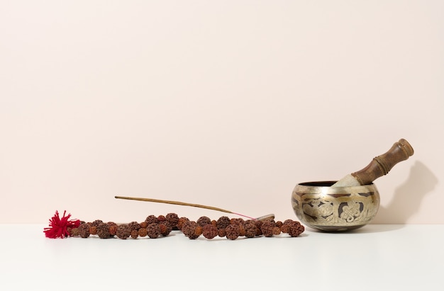 Copper singing bowl and wooden clapper on a white table. Musical instrument for meditation, relaxation, various medical practices related to biorhythms, normalization of mental health