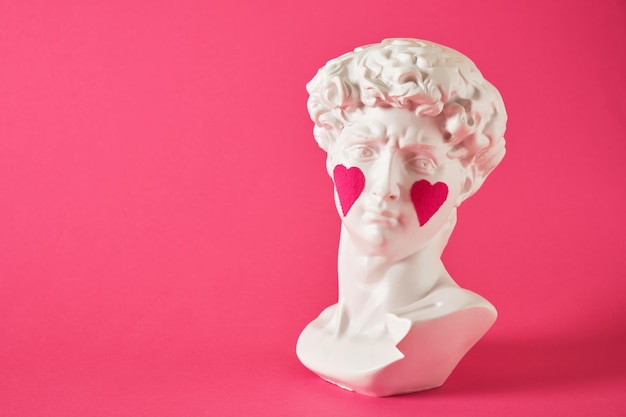 Copy of head of antique statue of David with pasted pink hearts on his cheeks a bright pink background