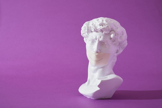 Copy of head of antique statue of David with sealed mouth purple background trendy colors smile painted on tape