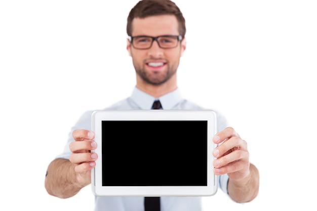 Copy space on digital tablet. Cheerful young man in formalwear and glasses showing his digital tablet and smiling while standing isolated on white background