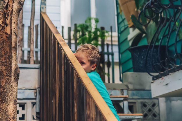 Copy Space lifestyle funny photo little boy move sit wood stairs outside handrails look for smile facial expression play hide peek out from behind Concept new children game education behavior