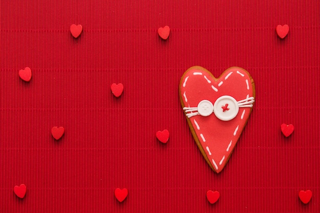 Copy space on red background with lots of small red hearts and a big gingerbread red heart on the right with white sugar buttons on its red covering