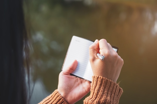 Copy space of woman hand writing down in white notebook with sun light background.