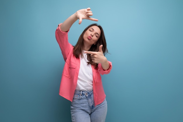 Coquette brunette woman in a pink shirt makes a photo using a phone on a studio background