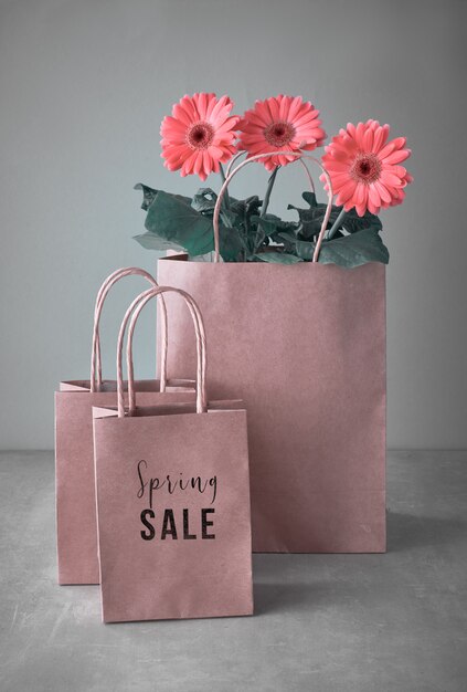 Coral gerbera daisy flowers and craft papper shopping bags on neutral background, text 