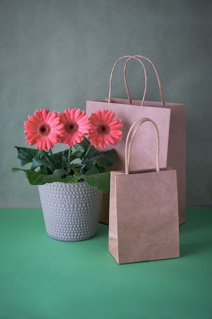 Coral gerbera daisy flowers and craft papper shopping bags on paper covered background, copy-space