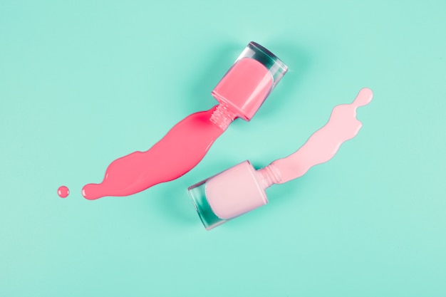 Coral and pink spilled nail polish bottles on mint background