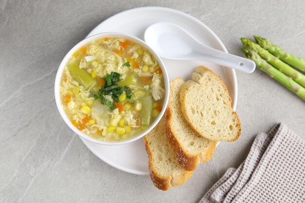 Corn and asparagus with egg drop soup in white bowl and crispy bread