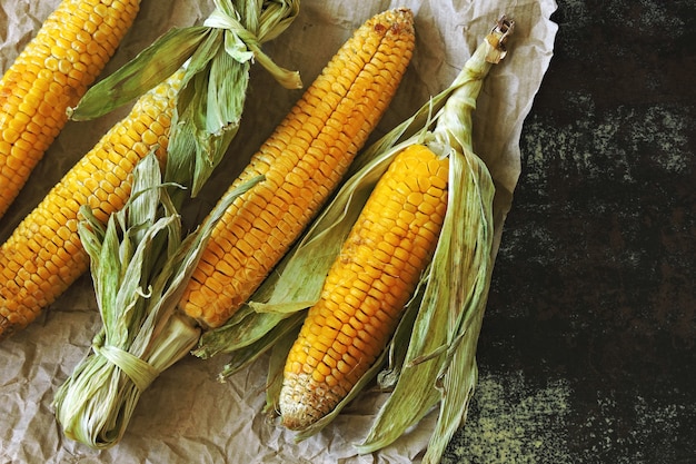 Corn cobs baked in the leaves on a baking sheet.