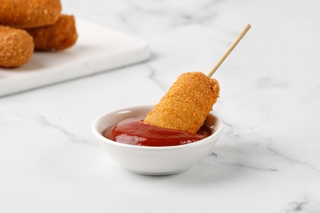 Corn dog with ketchup red sauce on white marble background Fried sausage on a stick Sorn dog corndog