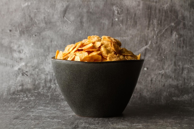 Corn flakes in a black bowl on stone background with copy space