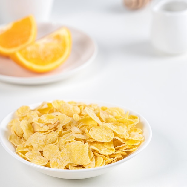 Corn flakes bowl sweeties with milk and orange on white background close up fresh and healthy breakfast design concept