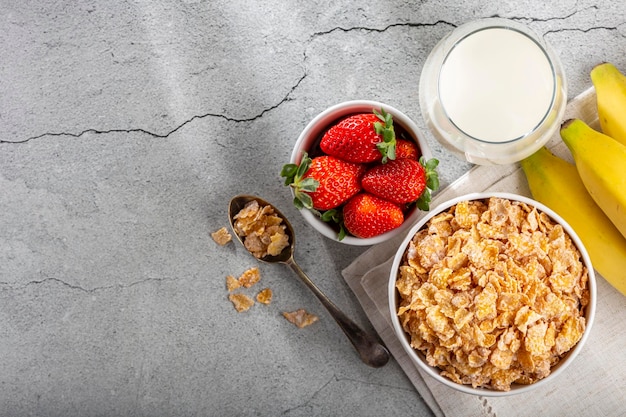 Corn flakes in the bowl with berries and milk on the table